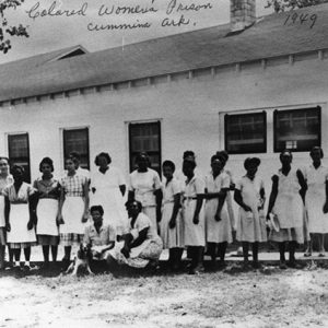 Group of African-American women in dresses and aprons outside single-story building