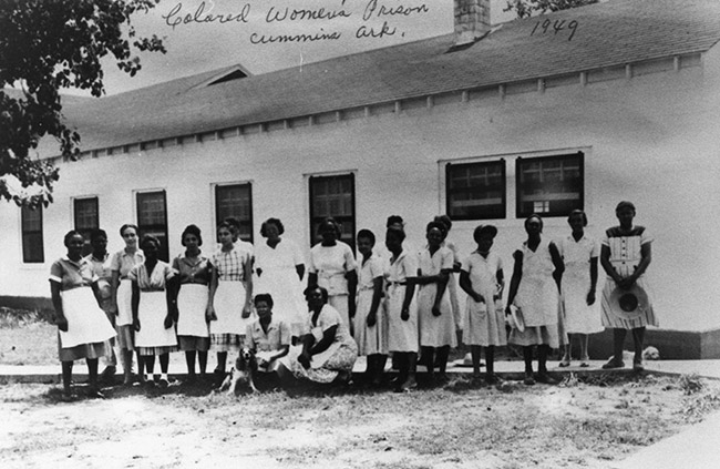 Group of African-American women in dresses and aprons outside single-story building