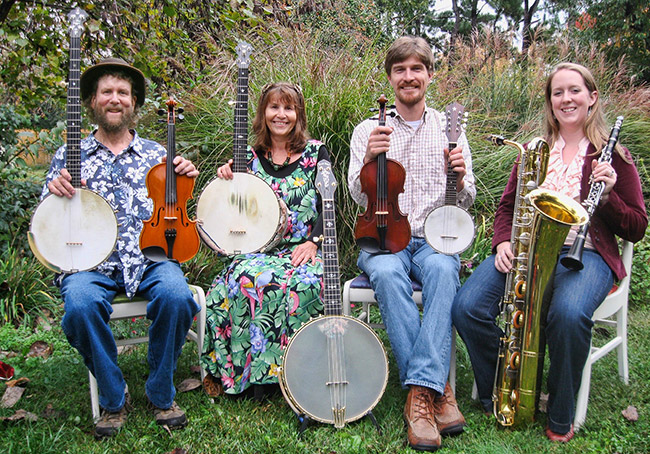 Two white men and two white women sitting outside with banjos fiddles and saxophone