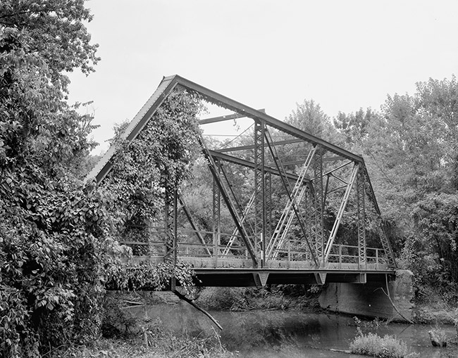 Steel truss bridge partially covered with ivy and concrete platform