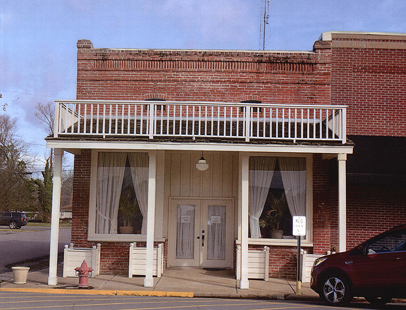 Red car parked outside brick storefront with covered entrance and balcony