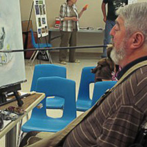 White man in chair painting on a canvas using paintbrush in his mouth