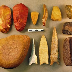 Rock arrowheads and stone tools laid out together on table with small ruler