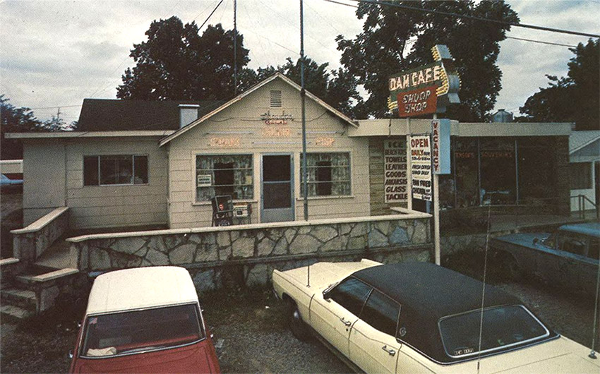 Cars parked outside "Dam Cafe" building with neon sign