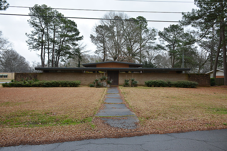 Brick building with flat roof with sidewalk and front yard