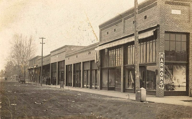"Harmon's" store with display windows and brick storefront buildings on dirt street