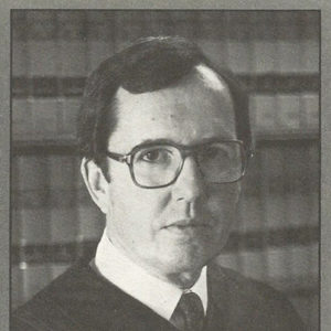 White man with glasses in judge's robes on campaign card