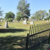 Gravestones in cemetery with black iron fence and trees