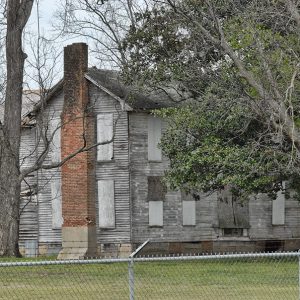 Abandoned large two-story house with brick chimney behind fence