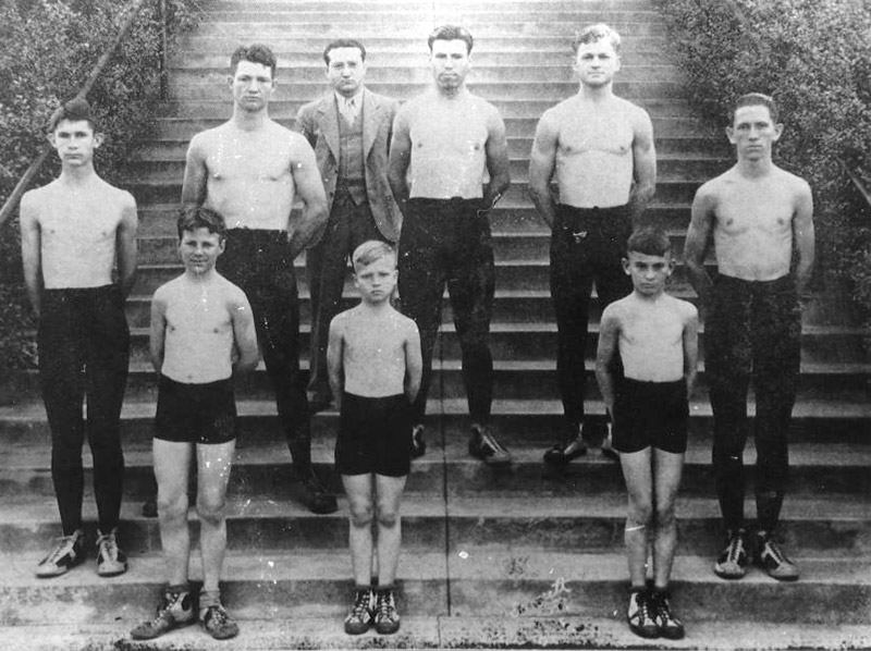 Group of young white men and boys posing shirtless on steps with white man in suit