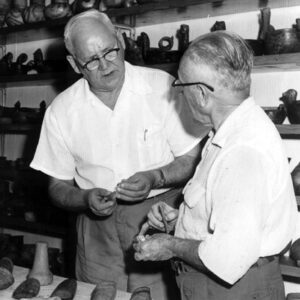 Two old white men with glasses analyzing bits of pottery in artifact storage room