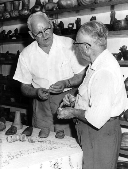Two old white men with glasses analyzing bits of pottery in artifact storage room