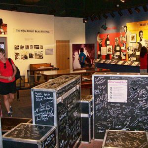 White women in museum with autographed instrument cases and display cases