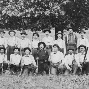 Group of white men with guns posing in field with trees in the background