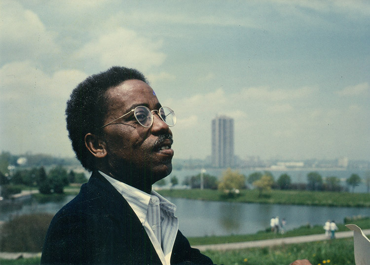 African-American man with glasses speaking with cityscape behind him