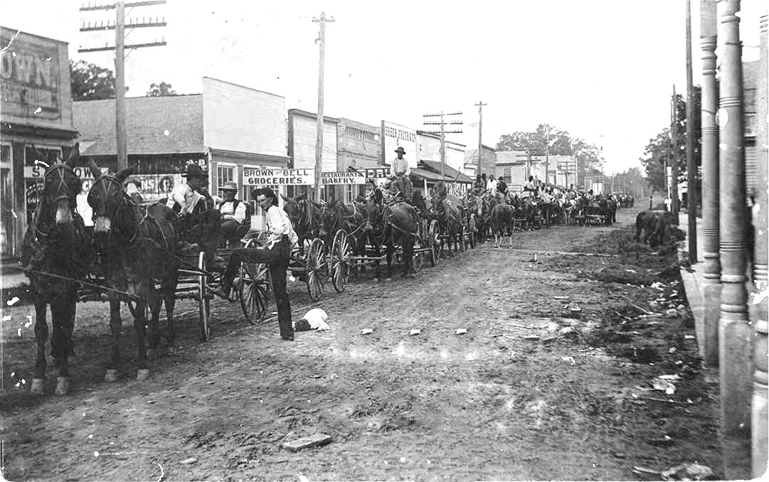Men driving horse drawn wagons on town street