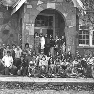Group of white children and teenagers posing on steps of stone school house with arched entrance way