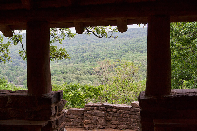 Interior of wood and stone pavilion looking out onto tree covered hill