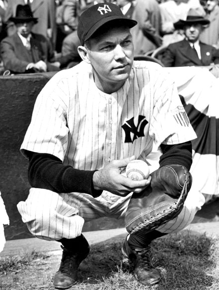 White man crouching in a New York Yankee uniform with ball and glove and spectators in background
