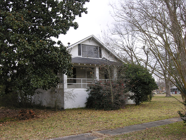 Small two-story white house with covered porch and trees
