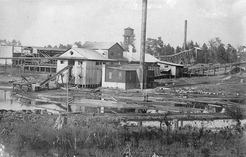 Industrial buildings with smoke stacks and water tower on muddy ground