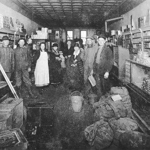 Group of white men and women standing in store amid various goods on floor and shelves