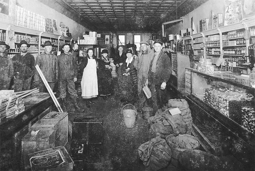 Group of white men and women standing in store amid various goods on floor and shelves