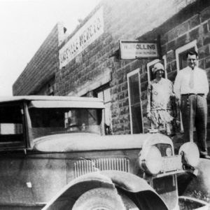 White man and woman standing outside brick building with car