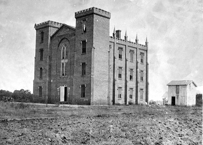 Tall castle like building with arched windows and small shed