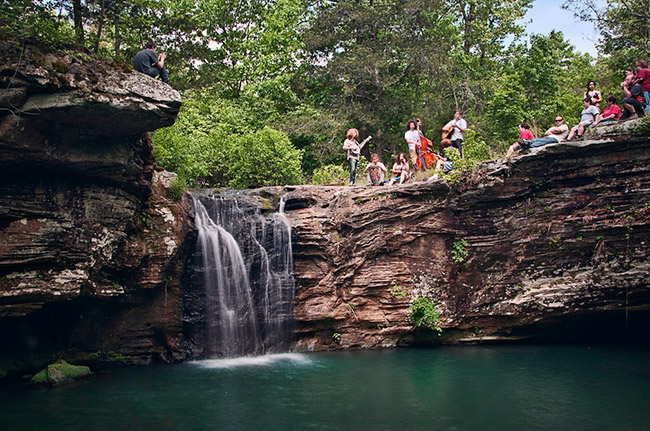 White men women and children standing on rock wall above waterfall and pool of water