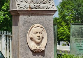Bust of young white boy on engraved stone monument with trees and other monuments in the background