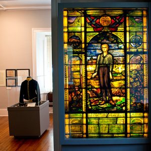 Young white boy on stained glass window in museum with military uniform in glass case
