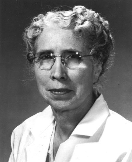 Old white woman with curly hair and glasses in white coat