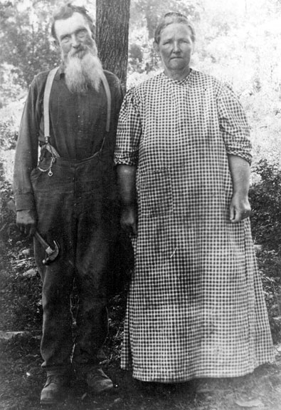 Old white man in overalls with hammer and old white woman in checkered dress