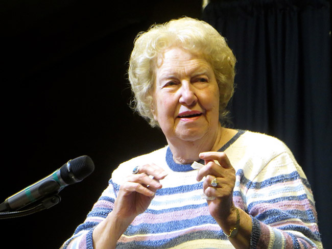 Old white woman speaking at microphone in striped sweater