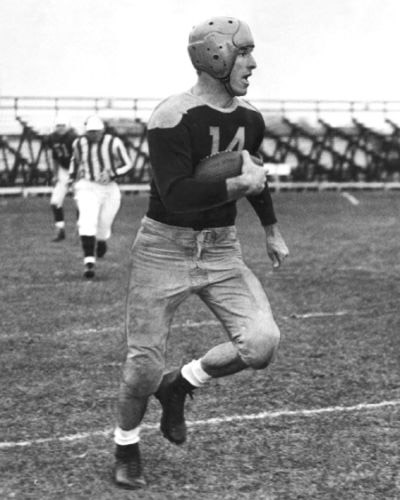 Young white man in uniform and helmet running with football