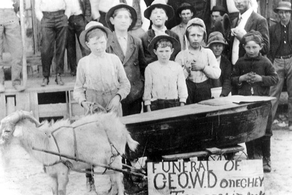 White men, women, and children with toy horse and small coffin with sign "Funeral of Geo. W. Doneghey"