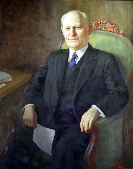 Old white man in suit with a blue tie sitting in a green chair