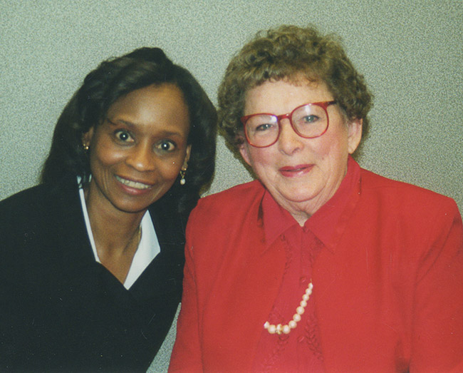 African-American woman smiling with white woman in red glasses smiling in red suit