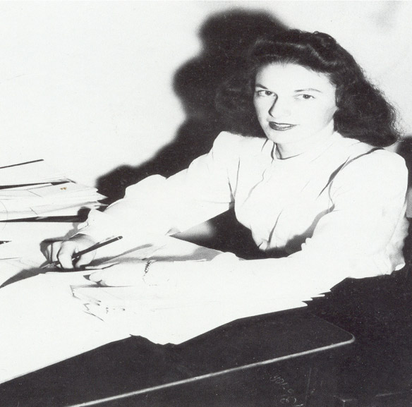 White woman with white blouse and dark hair writing at desk