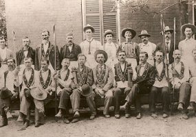 Group of white men in Masonic garb outside brick building