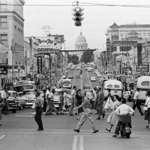 busy city intersection with cars and people, view of state capitol in background