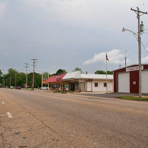 Single-story storefronts and two-car garage building with flag pole on street