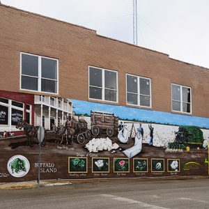 Two-story storefront with mural depicting horse drawn wagon cotton pickers in field and harvester