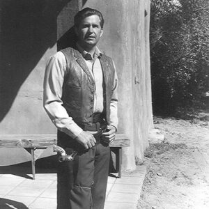 White man on film set standing in vest with gun belt