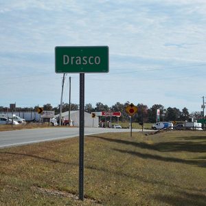 "Drasco" sign on multilane road with service station in the background