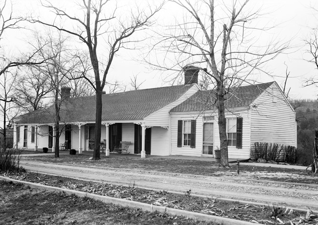 Single-story white house with covered porch with columns and driveway and bare trees in front