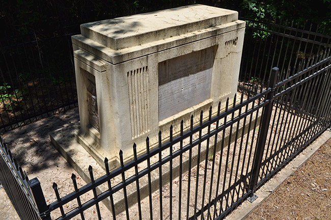 Stone monument with engraved plaque inside iron fence