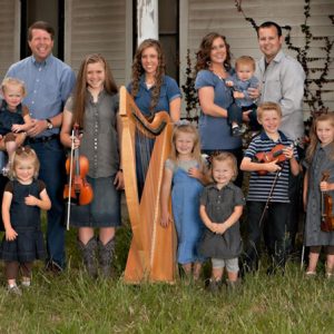 A group of white men women and children holding musical instruments with a house behind them