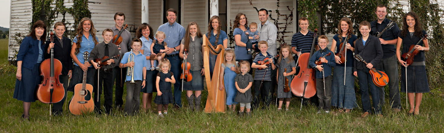 A group of white men women and children holding musical instruments with a house behind them